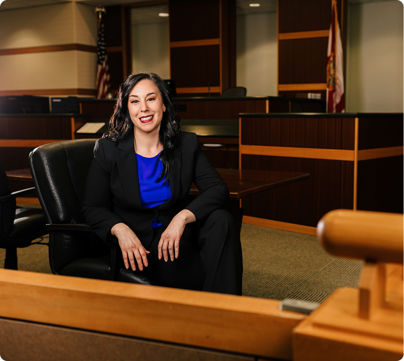 Connecticut Estate Planning Attorney in Courtroom Professional female estate planning attorney in black suit with blue blouse smiling confidently in courtroom setting